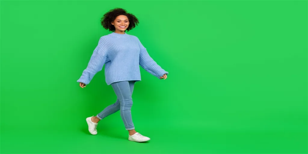 Foto a grandezza naturale di una bella donna ondulata che indossa maglione, jeans e stivali, isolata su sfondo verde