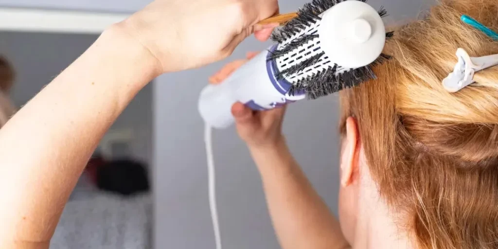 Une fille lisse ses cheveux avec une brosse-sèche-cheveux Volumebrush