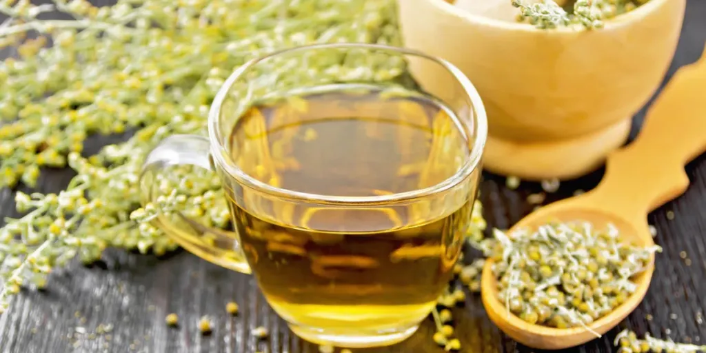 Gray wormwood herbal tea in a glass cup, dry sagebrush flowers in spoon