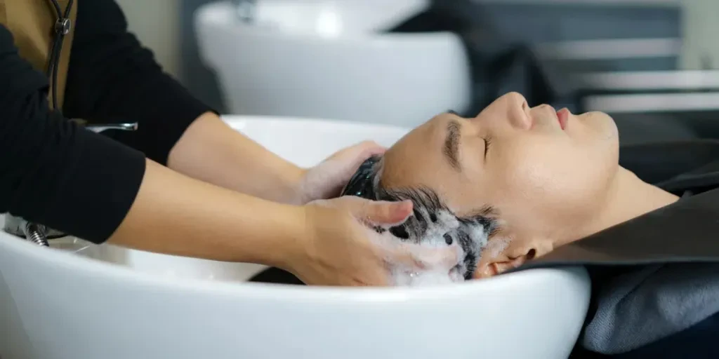 El peluquero está aplicando champú y masajeando el cabello de un cliente.