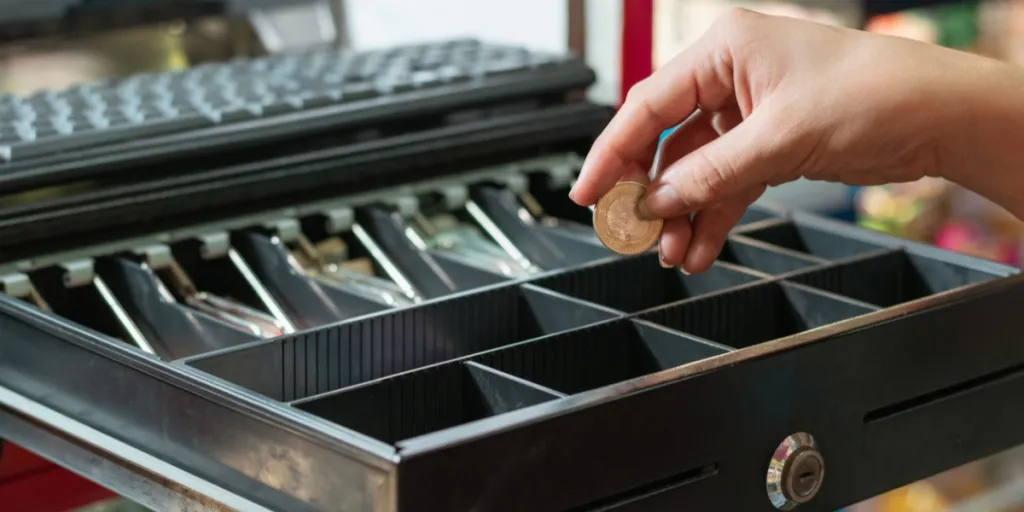 Mano colocando moneda en una caja registradora