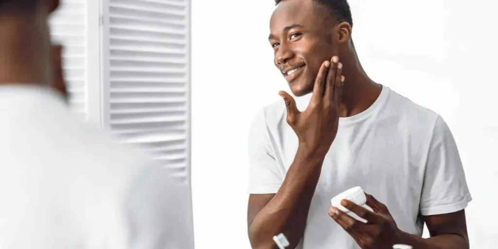 Handsome Black Man Using Facial Cream Moisturizing And Caring For Face Skin Standing