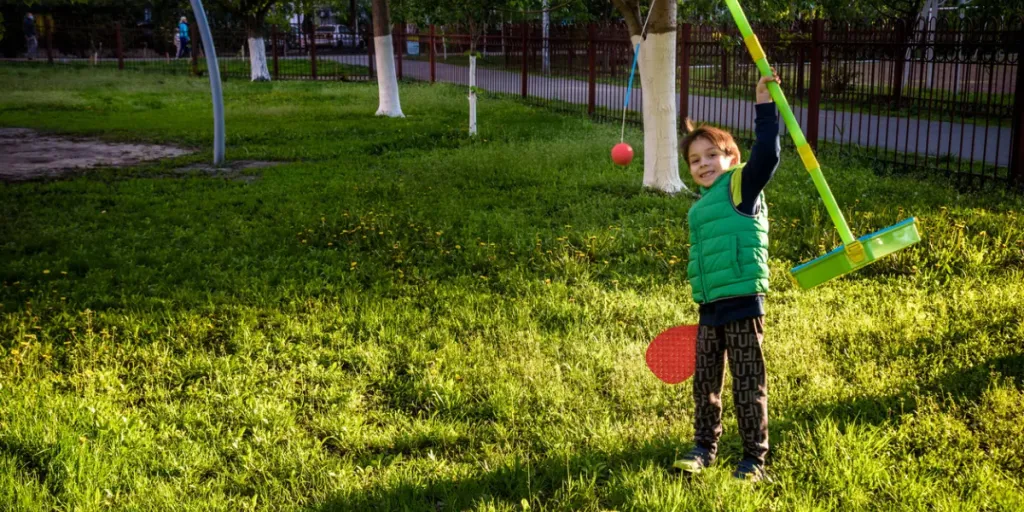 Anak laki-laki yang gembira sedang memainkan permainan ayunan bola tetherball di perkemahan musim panas