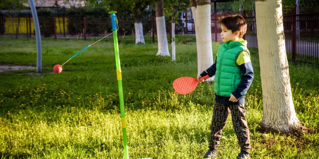 Anak laki-laki yang gembira sedang memainkan permainan ayunan bola tetherball di perkemahan musim panas1