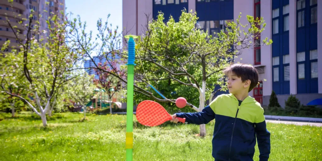 เด็กชายมีความสุขกำลังเล่นเกม Tetherball Swing Ball ในแคมป์ฤดูร้อน2