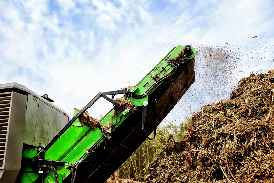 Une énorme machine libère des déchets de jardin déchiquetés dans un tas de compost