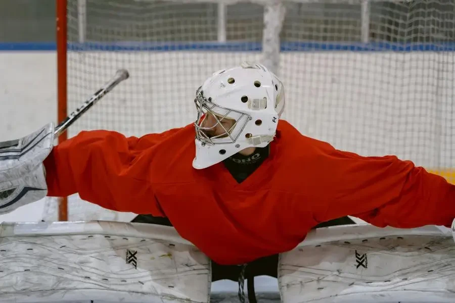 Ice hockey goalkeeper in red jersey performing a save on the rink