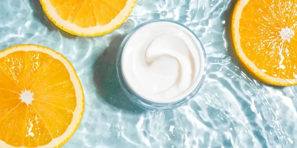 Tarro de crema cosmética con vitamina C sobre un fondo de agua azul transparente salpicada con rodajas de naranja