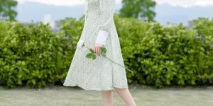 Dame en robe fleurie blanche et verte tenant une fleur