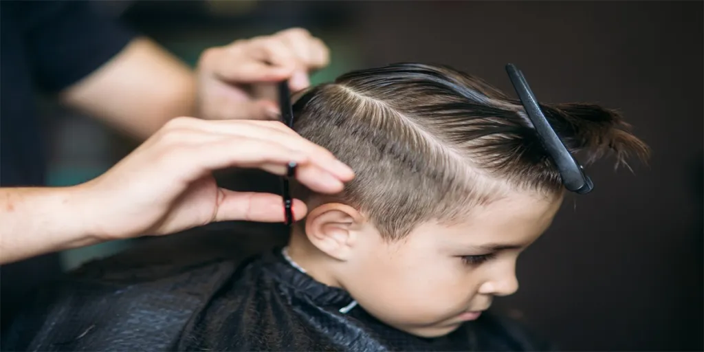 Anak laki-laki kecil sedang potong rambut di tukang cukur duduk di kursi