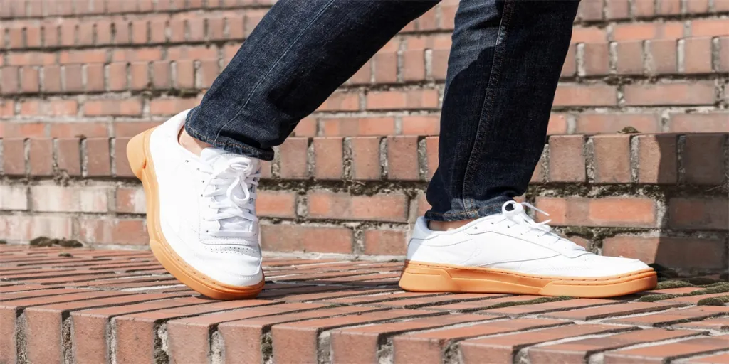 Male legs in jeans and white sneakers close up against the background of a brick staircase