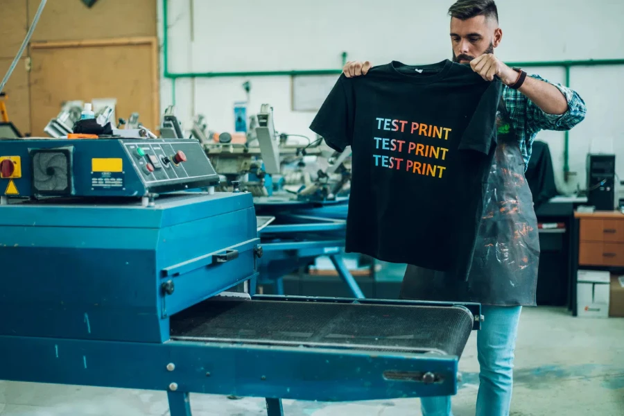 Male worker using a drying oven for t-shirt after using a printing machine in a workshop