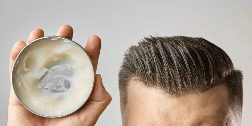 Hombre aplicando arcilla, pomada, cera, gel o espuma de una caja redonda de metal para peinarse después de un corte de pelo en la peluquería