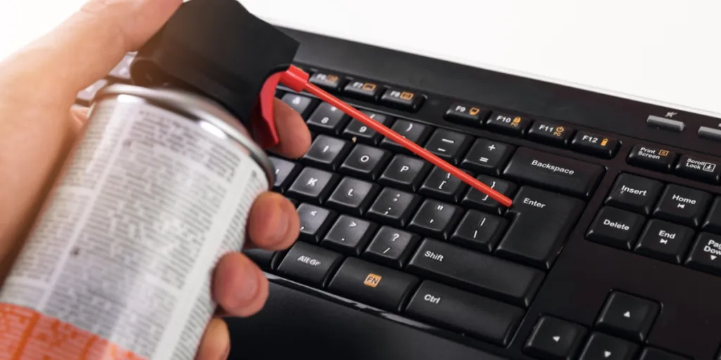 Man holding a can of air duster near a keyboard