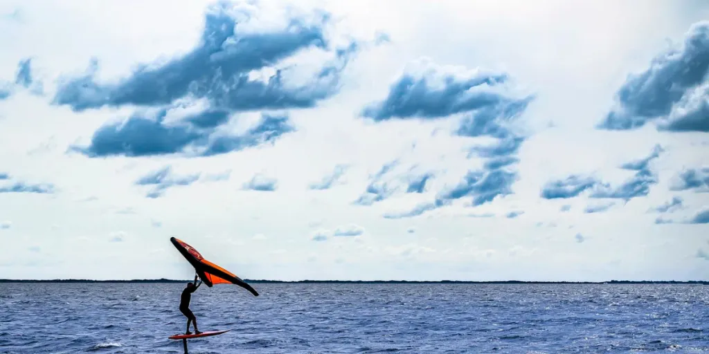 Mann in Silhouette Winging oder Wingfoiling mit leuchtend orange Rig auf leicht