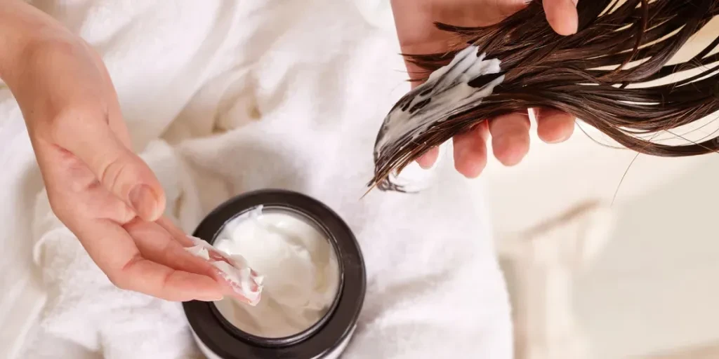 Person applying hair mask to wet hair, close-up of hands and hair