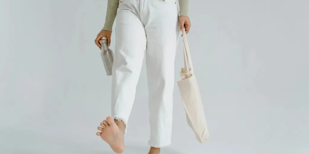 Person walking barefoot with reusable cloth bag and water bottle, promoting zero waste lifestyle by Tima Miroshnichenko