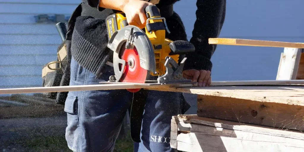 Portret van een timmerman die buiten hout zaagt met een cirkelzaag, waarbij hij veiligheidsuitrusting draagt