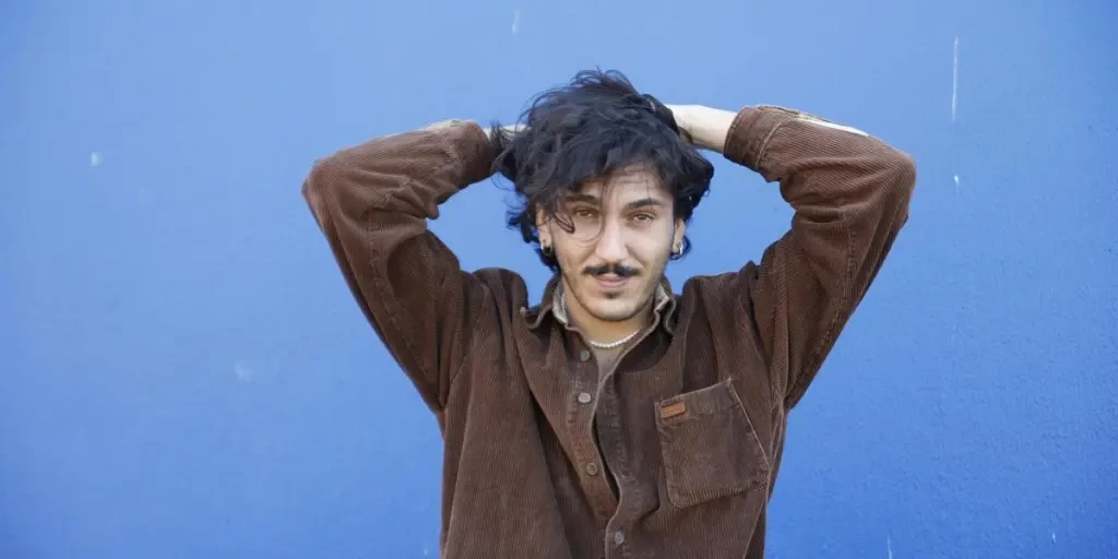 Portrait of a man in a brown shirt standing against a vibrant blue background