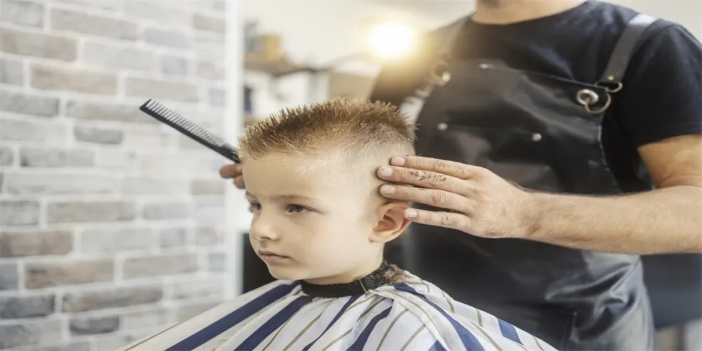 Potret seorang anak laki-laki kecil yang menggemaskan di kursi di tempat pangkas rambut yang sedang mendapatkan potongan rambut baru