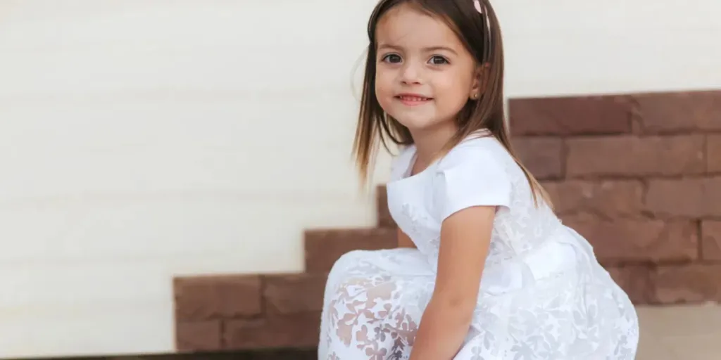 Portrait of beautiful little girl in white dress sitting on stairs by home