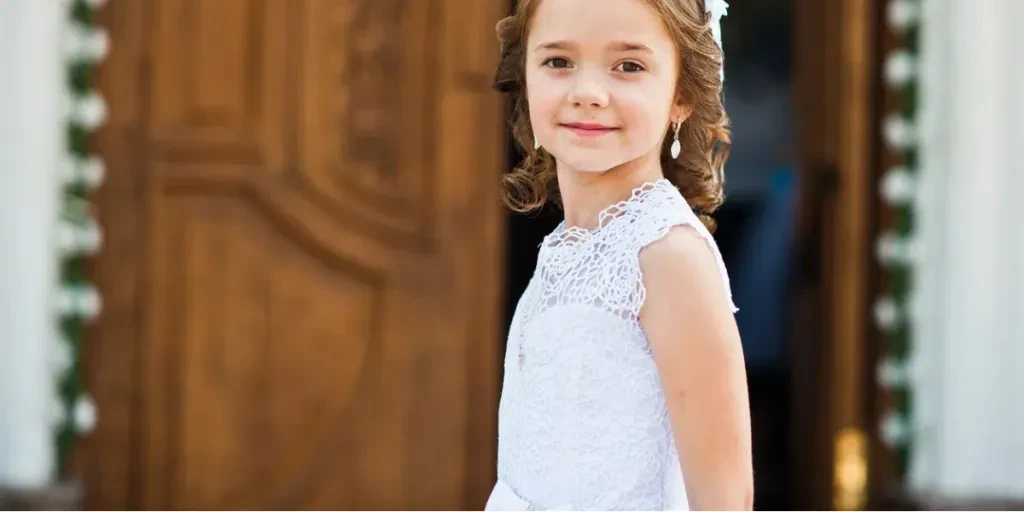 Retrato de una linda niña con un vestido blanco y una corona en el fondo de la puerta de la iglesia de la primera comunión