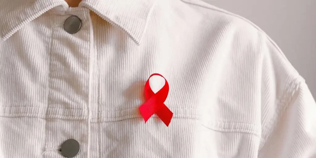 Red ribbon for HIVAIDS awareness pinned on a white shirt symbolizing support and solidarity