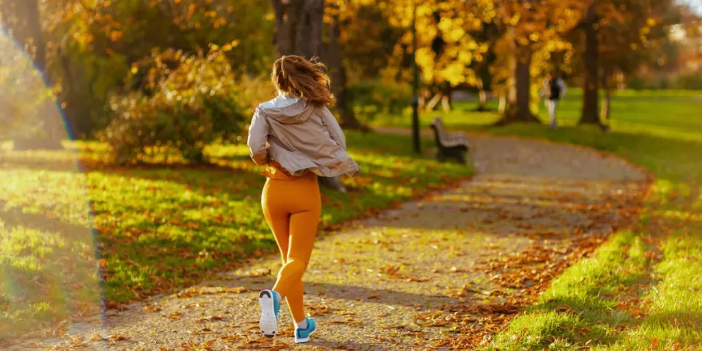 Parkta koşu yapan, spor kıyafetleri giymiş, modaya uygun bir kadının arkasından görülüyor