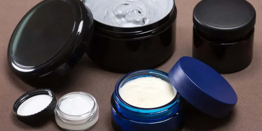 Several jars of different sizes filled with creams on brown background