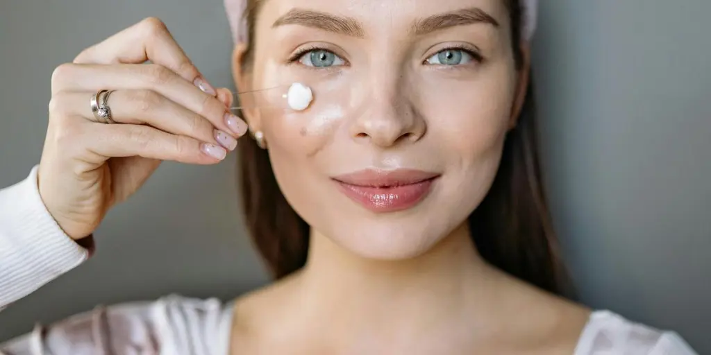 Donna sorridente che applica la crema per il viso per la routine di cura della pelle