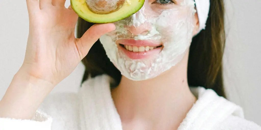 Femme souriante avec un masque facial tenant un avocat pour les soins de la peau dans un cadre de spa