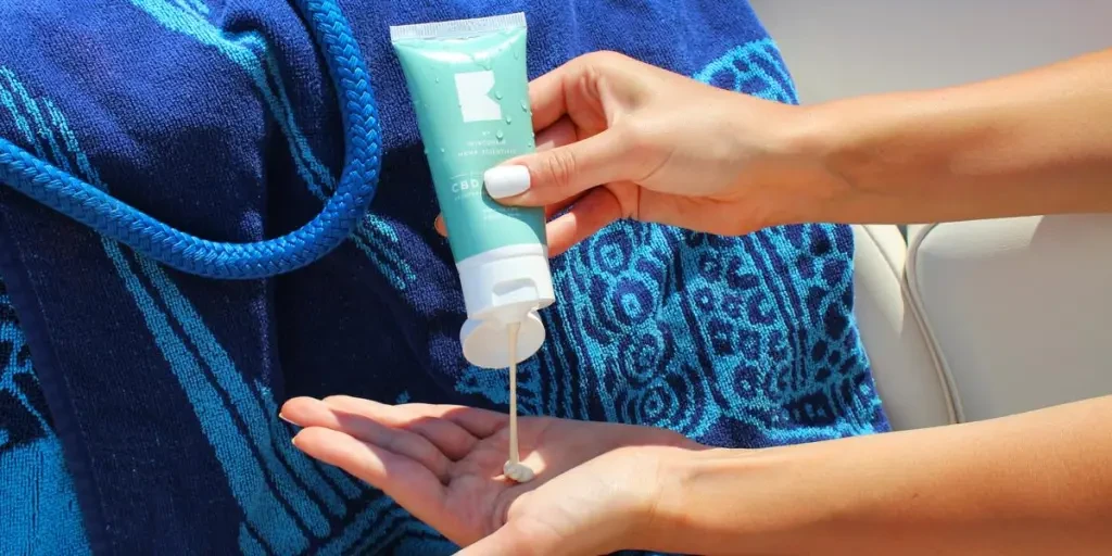 CBD-Lotion in die hohle Hand drücken auf einem Boot mit Strandtuch und Seil von BATCH