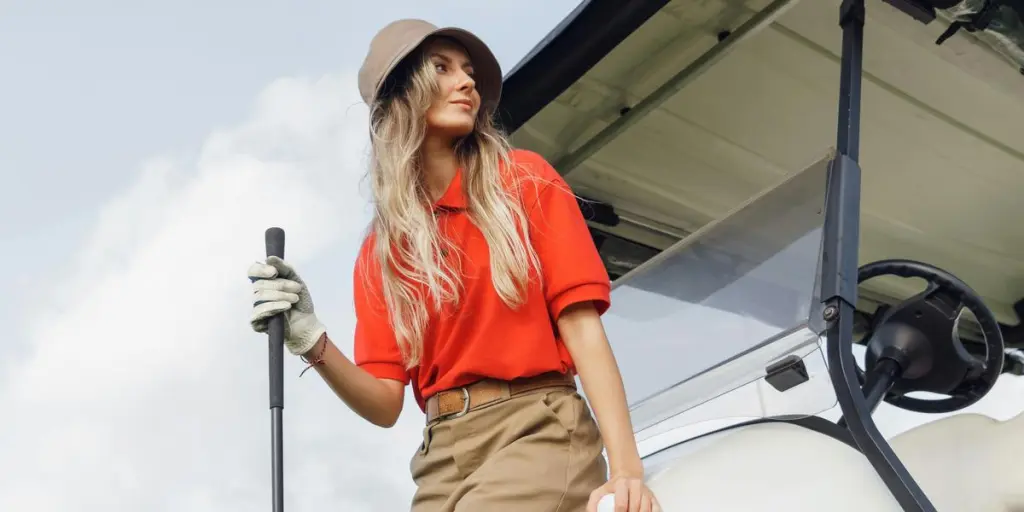 Stilvolle Frau in einem Golfwagen, mit einem Schläger in der Hand, vor einem hellen Himmel