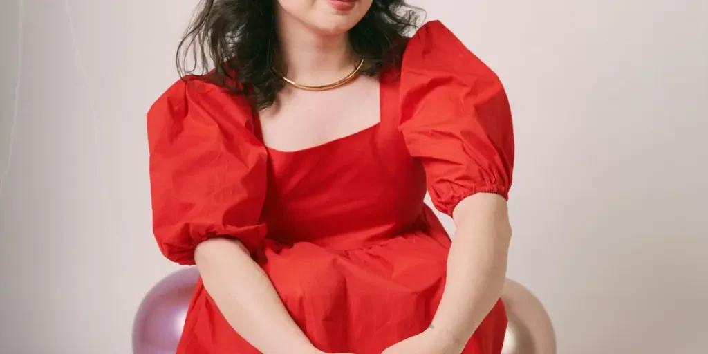 Stylish young woman in red dress poses elegantly indoors. Trendy fashion portrait