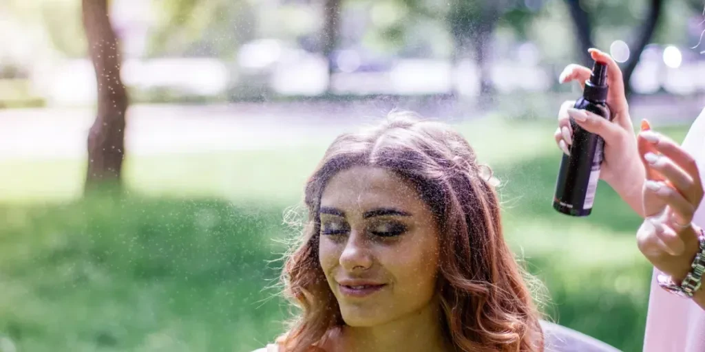 Estilista borrifando spray de cabelo nos cabelos de uma jovem