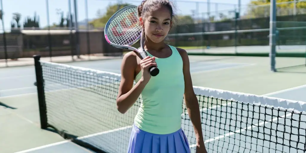 Açık havada tenis raketiyle poz veren genç kız, spor kıyafetlerini ve özgüvenini sergiliyor