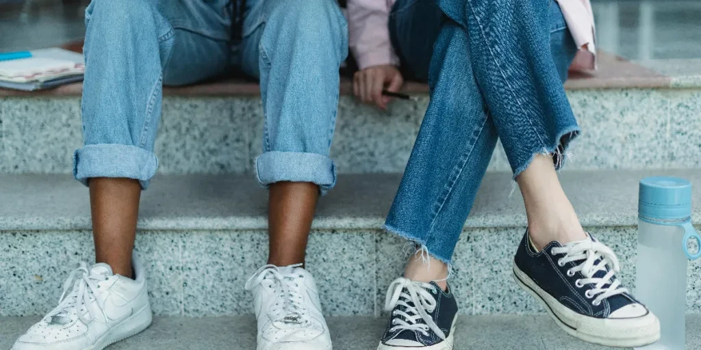 Two friends in jeans and sneakers sitting on an outdoor staircase, symbolizing casual student life and friendship by Zen Chung