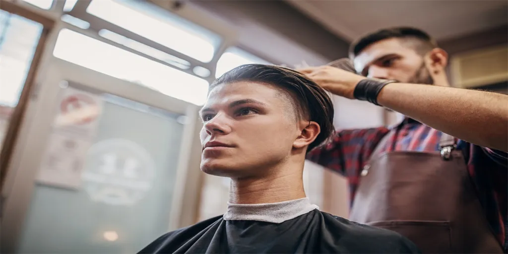 Dos hombres, un joven siendo cortado el pelo por un peluquero mientras está sentado