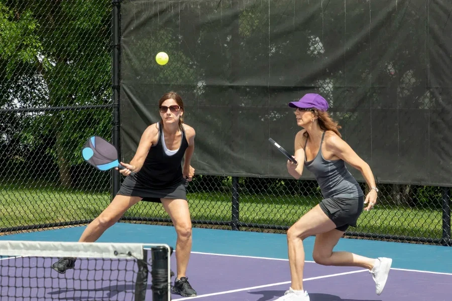 Due giocatori di pickleball si preparano a restituire la palla su un campo da pickleball suburbano durante l'estate