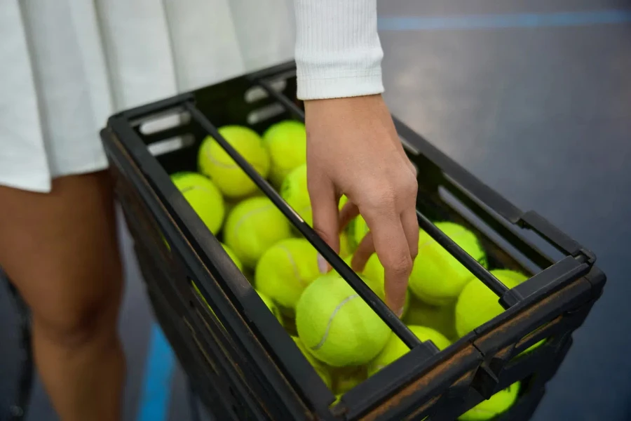 Mujer irreconocible sacando pelotas de tenis de una canasta de hierro en la cancha