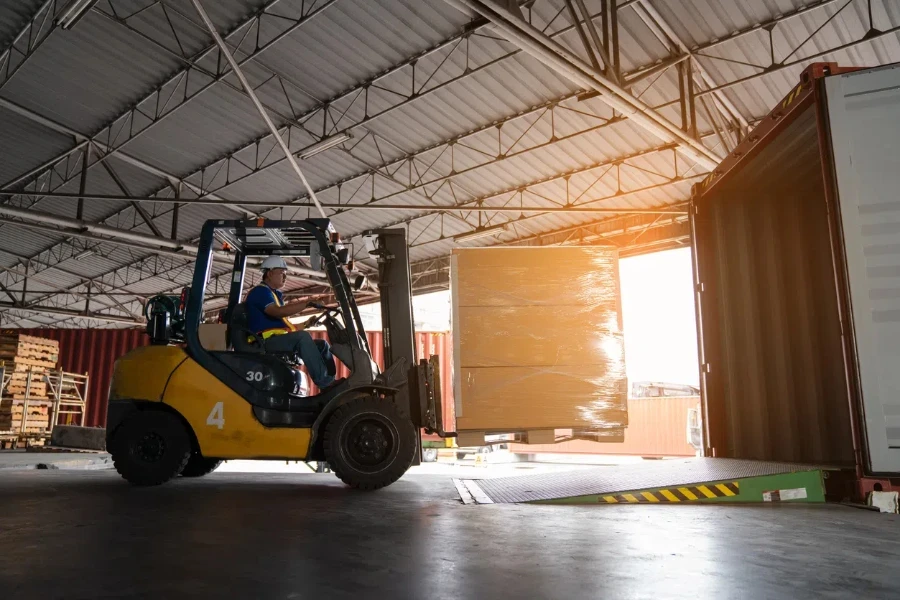 Warehouse worker driver in uniform delivery and loading pallet product by forklift