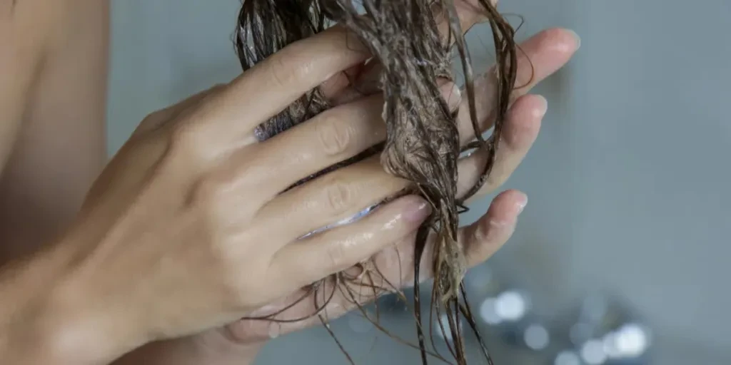 Woman applaying conditioner on her wet tangled hair in the shower cabin