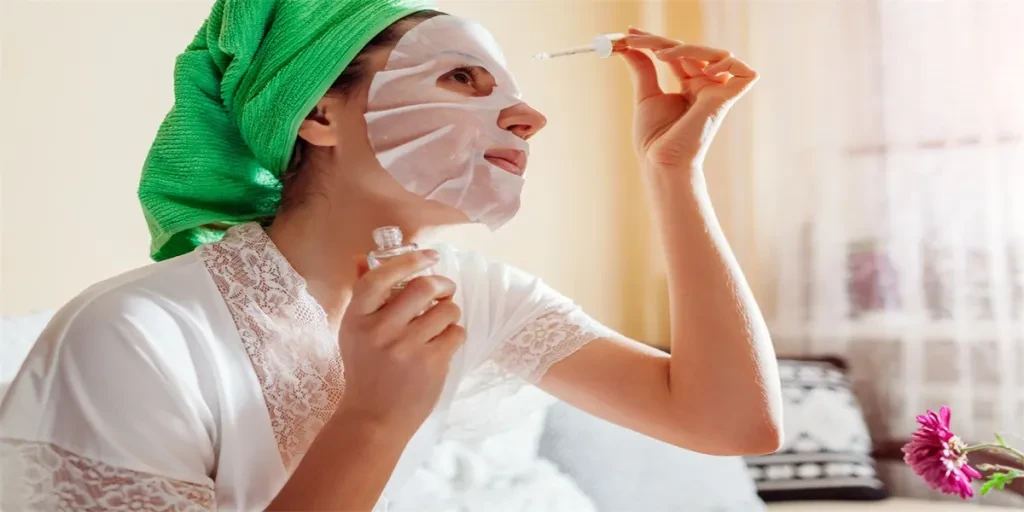 Mujer aplicando suero facial de ácido hialurónico con mascarilla y toalla después de la ducha