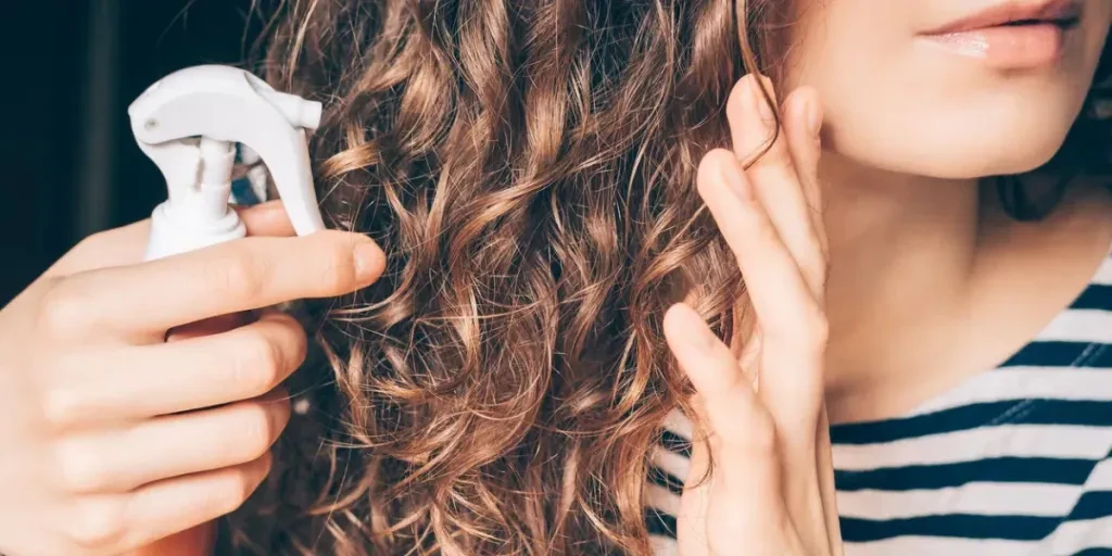 Woman applying spray on curly brown hair close-up