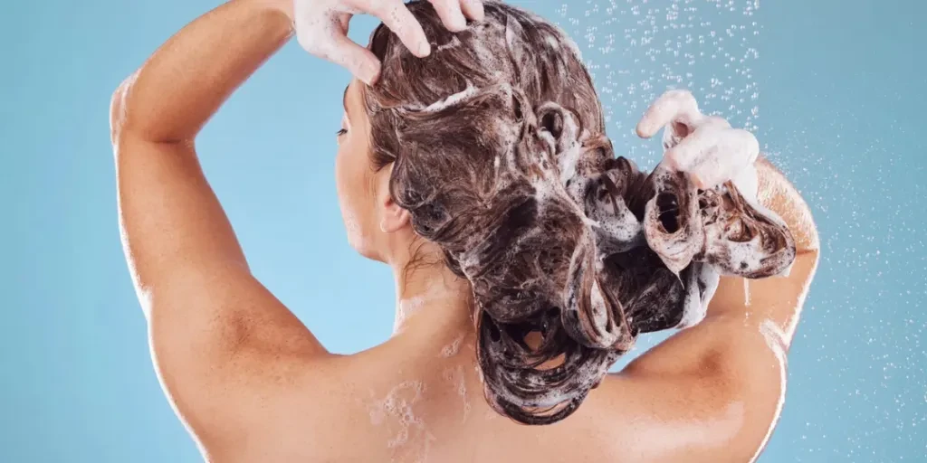 Woman, back and shampoo, haircare in shower and hygiene with water drops on blue background