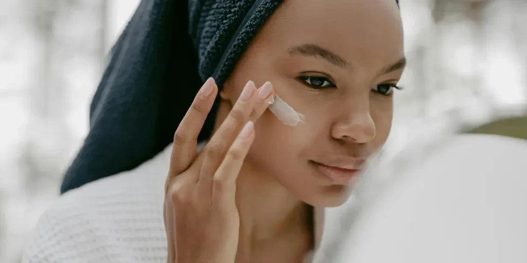 Une femme applique délicatement une crème pour le visage dans le cadre de sa routine de soins de la peau, en se concentrant sur une peau saine