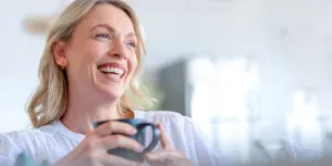 Woman holding coffee cup in house and showing smile lines