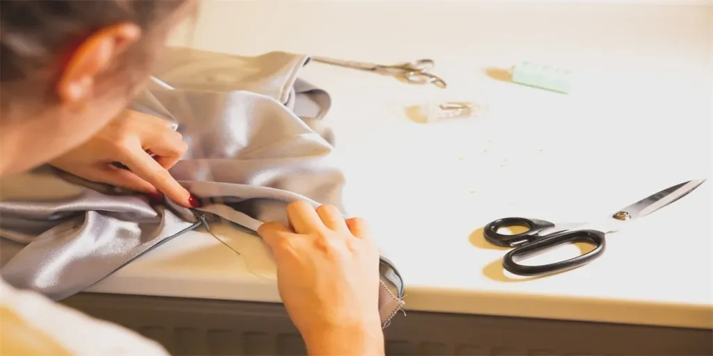 Woman is sewing a dress. Needle and thread in girl's hands