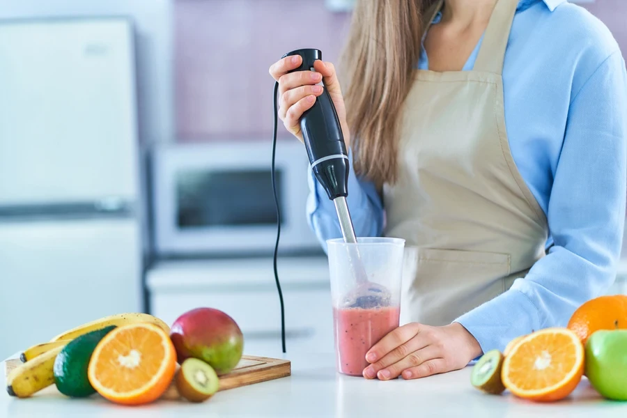 Woman making a fruit smoothie with a hand blender