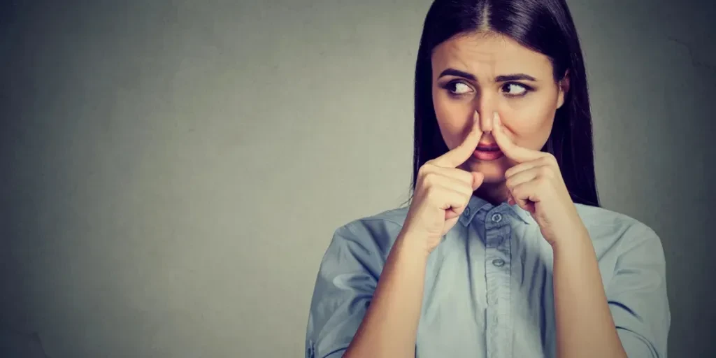 Wanita mencubit hidung dengan jari-jarinya, tampak jijik, ada sesuatu yang berbau tidak sedap, terisolasi pada latar belakang abu-abu